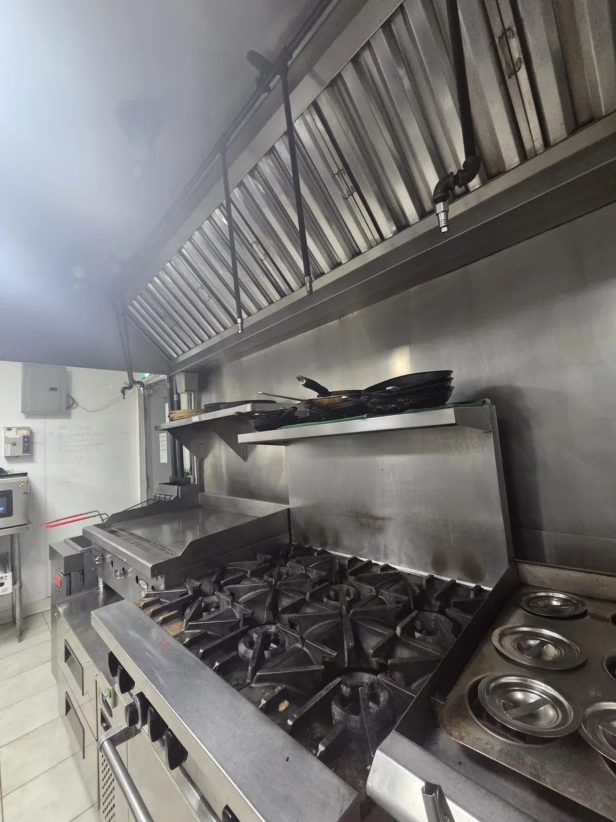 Commercial cooking equipment beneath a stainless-steel exhaust hood.