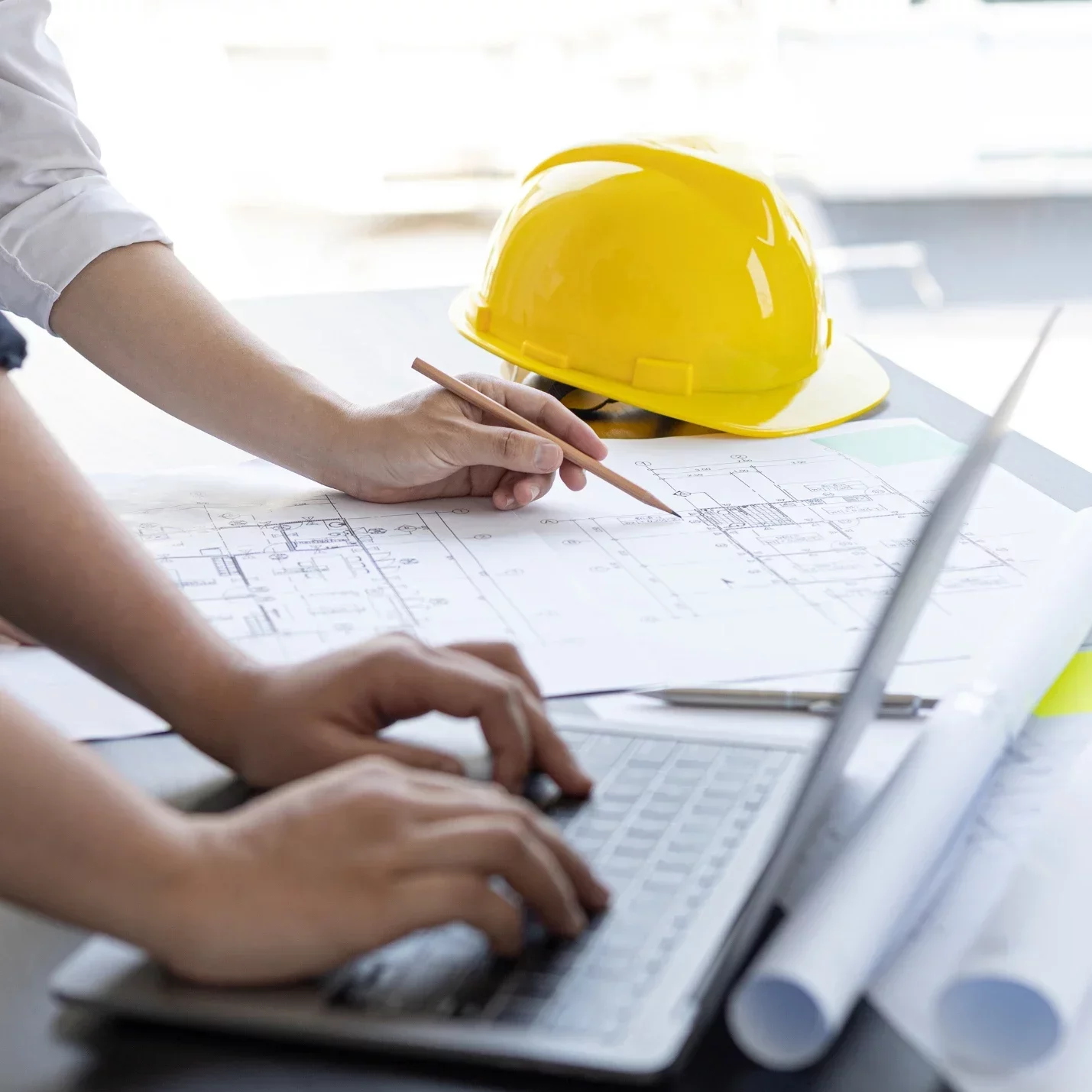 Building drawings, a laptop and a hard hat on a work table.