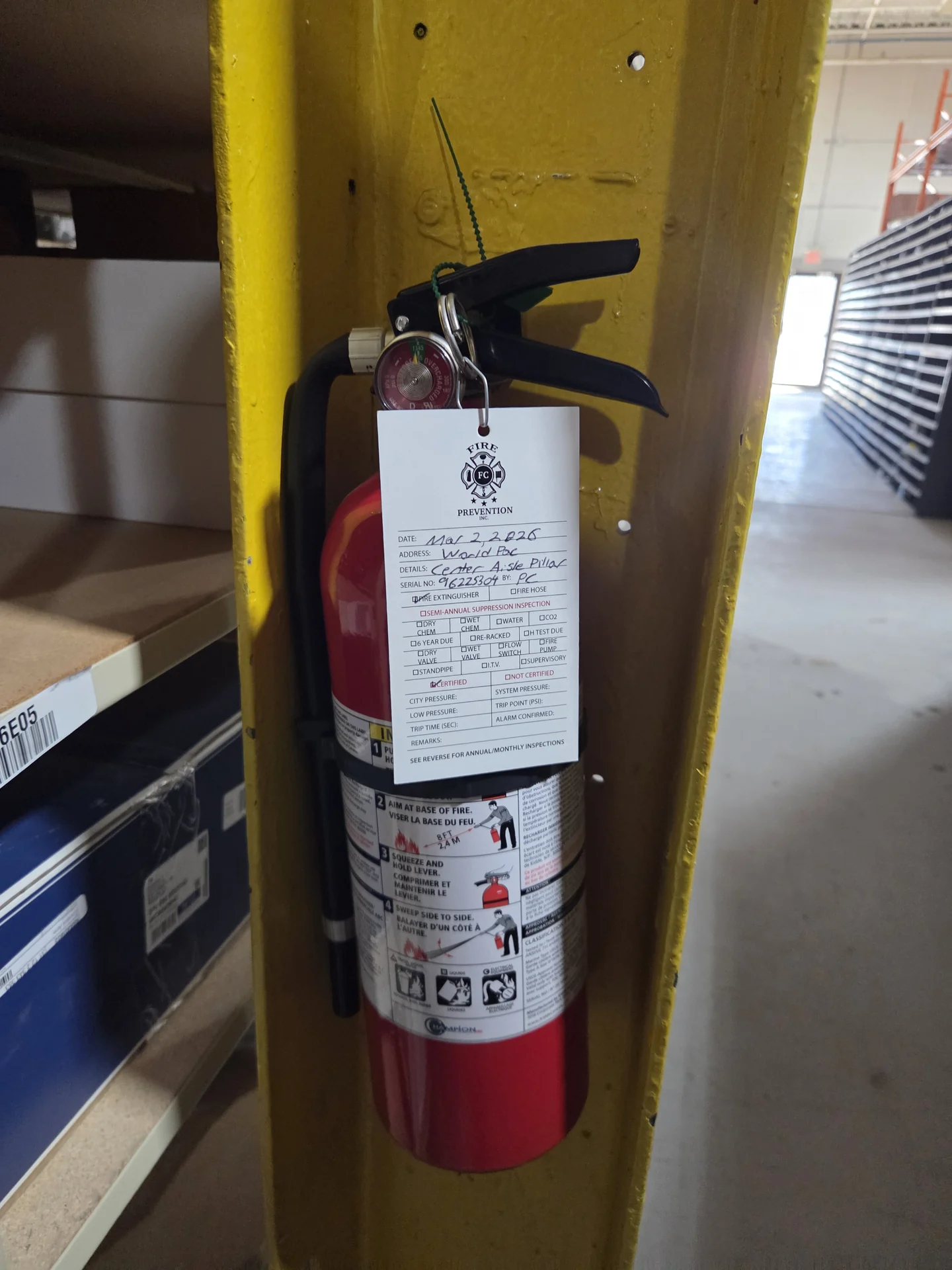 Complete portable extinguisher mounted on a yellow warehouse column, with FC Fire service tag.